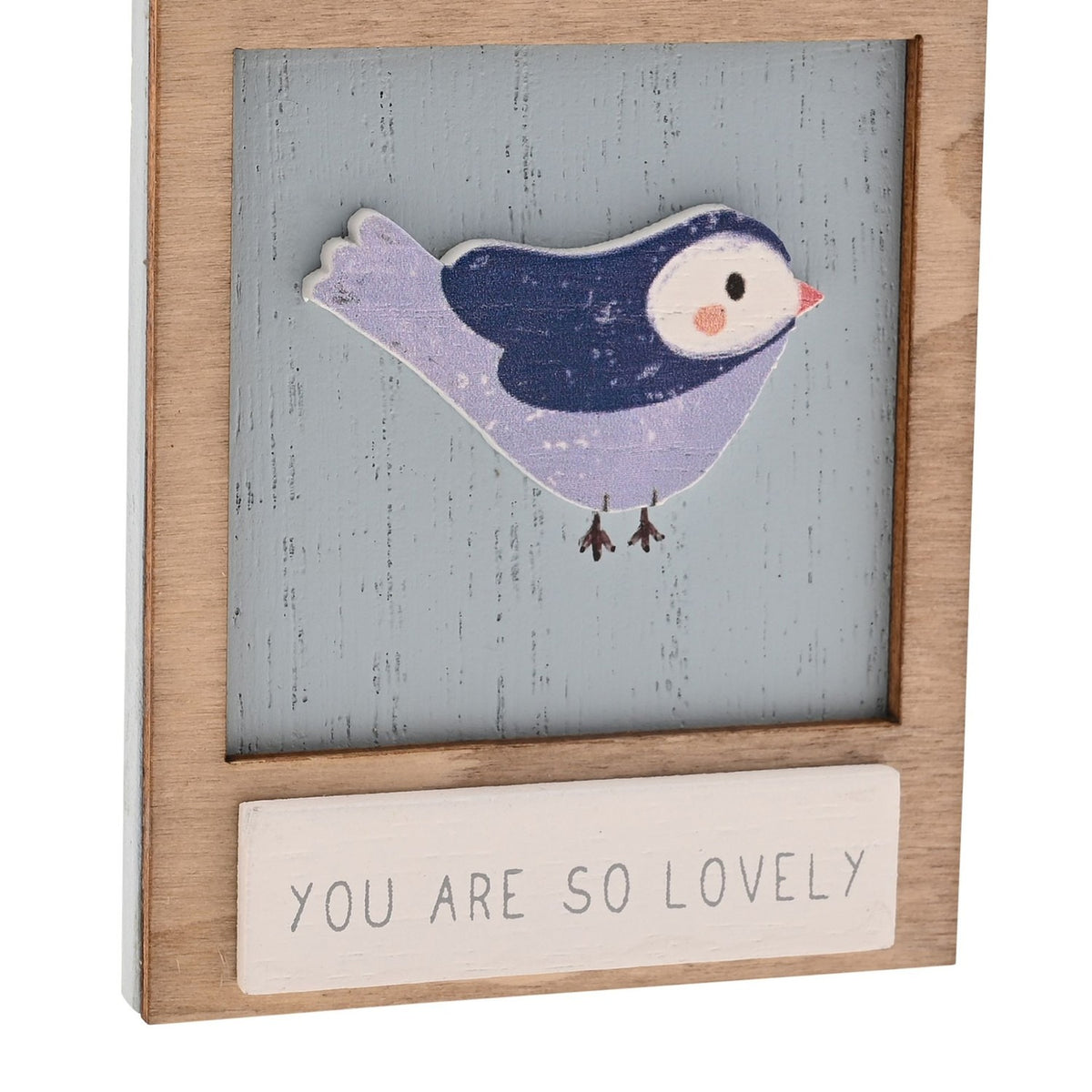 Wooden wall plaque featuring a raised lilac and navy bird with white face and pink beak on a weathered blue panel, framed in natural wood with "You Are So Lovely" in grey capitals below.
