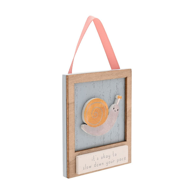 Wooden wall plaque with a raised orange and grey snail on a dusty blue background, natural wood frame, cream panel reading its okay to slow down your pace, hung by a coral ribbon.
