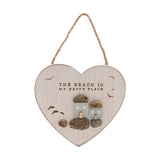 White heart-shaped wall plaque with jute cord, reading THE BEACH IS MY HAPPY PLACE above frosted sea glass cottages on pebble bases with gulls in flight, white background.