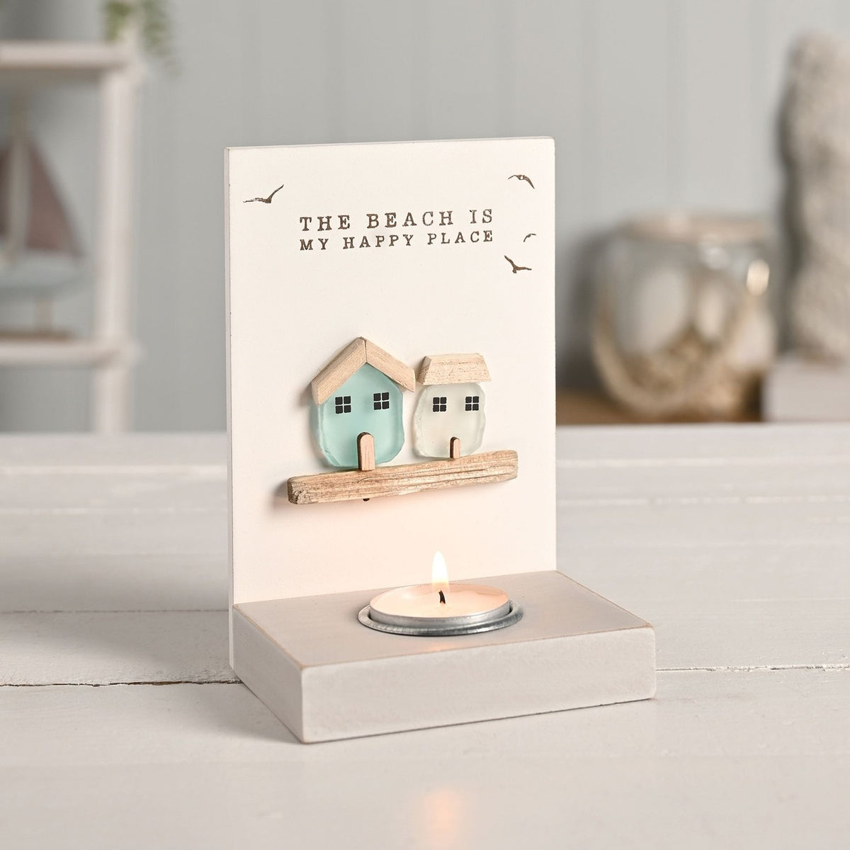 Cream tea light candle holder with "The Beach Is My Happy Place" text, seabird detail, and two sea glass houses in aqua and white above a lit tealight.