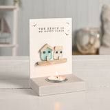 Cream tea light candle holder with "The Beach Is My Happy Place" text, seabird detail, and two sea glass houses in aqua and white above a lit tealight.
