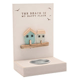 Cream wooden tea light candle holder with "The Beach Is My Happy Place" text, seabird motifs, and two sea glass houses in aqua and frosted white above a tealight slot, on a white background.