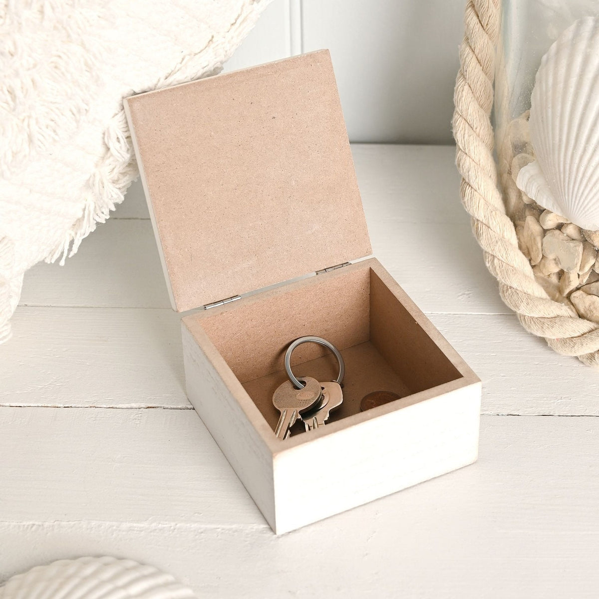 Square white wooden trinket box with hinged lid open, showing a plain interior holding a set of keys on a ring, styled with coastal décor.