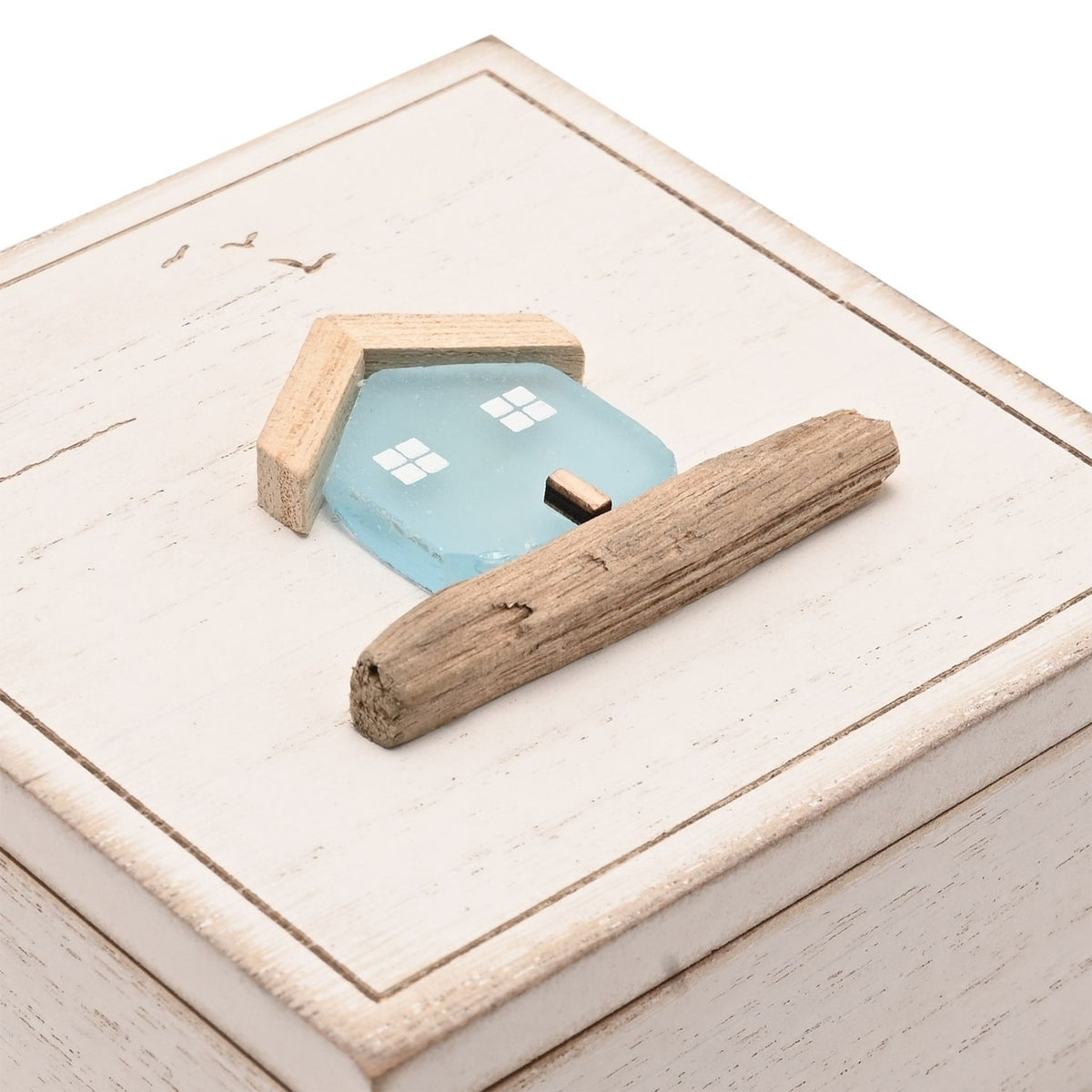 Square white wooden trinket box with hinged lid, lid detailed with a pale blue sea glass house, driftwood roof and base, and etched birds, on a plain background.