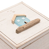 Square white wooden trinket box with hinged lid, lid detailed with a pale blue sea glass house, driftwood roof and base, and etched birds, on a plain background.