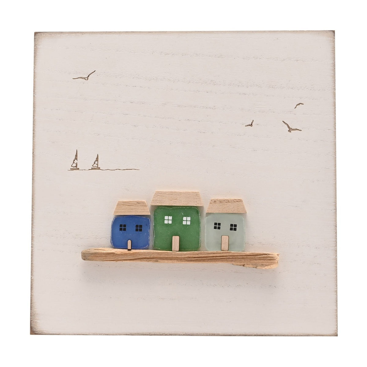 White square wall plaque with three sea glass cottages (blue, green, aqua) on a driftwood ledge, with engraved seagulls and sailing boats on a plain white background.