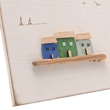 White square wall plaque with three glass cottage houses in cobalt blue, green and pale aqua on a wooden ledge, with engraved gulls and sailboats above.