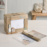 Driftwood photo trinket box with rectangular window, Beach text, pebble lighthouse, wooden house, and sea glass boat detail, shown open on a table with photo cards nearby.