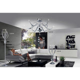 A modern living room with gray and white furniture, abstract wall art, large windows, and the Llamas 3 Light Table Lamp in polished chrome. A woman relaxes on a couch while another stands nearby.