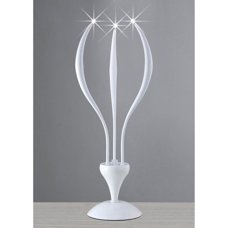 The Llamas 3 Light Table Lamp in gloss white features a sculptural design with three curved, petal-like arms ending in bright lights. Displayed on a striped surface against a plain gray background.