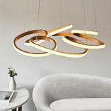 Lighting No.1 Tolmere Multi Spiral LED pendant in satin gold, its looped ribbon form glowing above a curved grey sofa and marble side table.