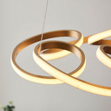 Close-up of Lighting No.1 Tolmere Multi Spiral LED Pendant in satin gold, showing looping metal ribbon coils with warm glowing inner edges against a pale wall.