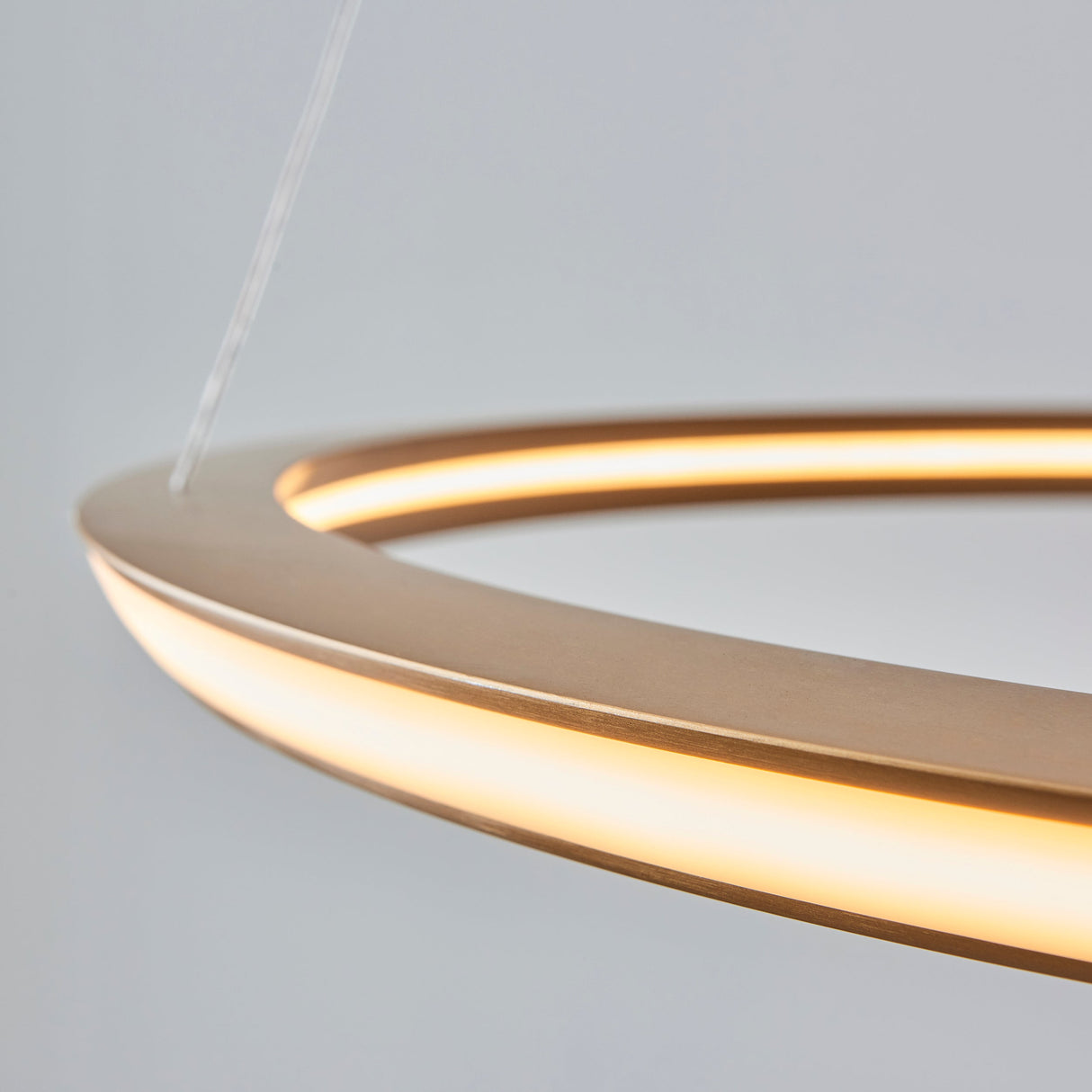 Close-up of Lighting No.1 Ashenhurst LED ring pendant in satin gold, showing the warm-lit circumference and slim metal profile against a pale background.
