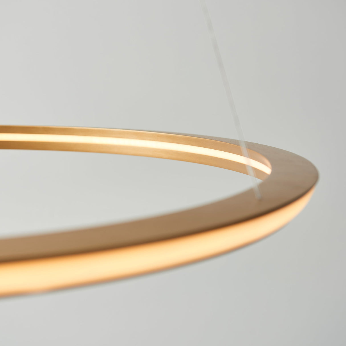 Close-up of the Ashenhurst LED Ring Pendant in satin gold, showing the illuminated metal ring and suspension wires against a light background.