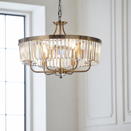 Calverdale Round Cut 6 Light Pendant in antique brass with clear faceted glass panels, suspended from a chain in a bright panelled room.