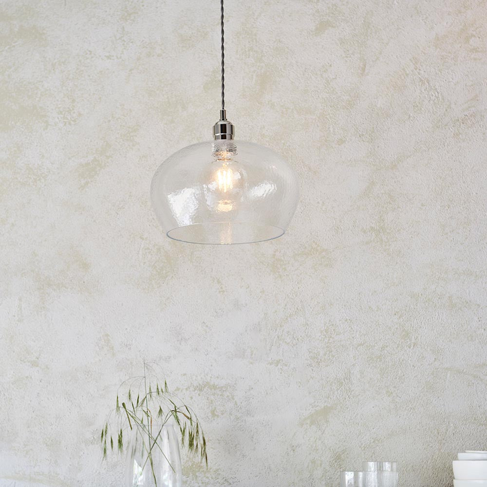Draywick Hammered Medium Pendant in clear hammered glass with bright nickel fitting from Lighting No.1, lit and hung against a pale plaster wall.