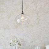Draywick Hammered Medium Pendant in clear hammered glass with bright nickel fitting from Lighting No.1, lit and hung against a pale plaster wall.
