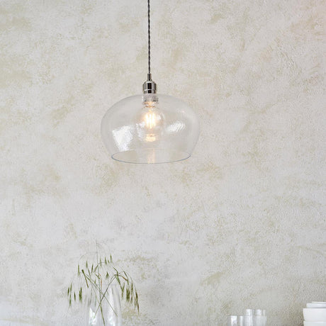 Draywick Hammered Medium Pendant in clear hammered glass with bright nickel fitting from Lighting No.1, lit and hung against a pale plaster wall.
