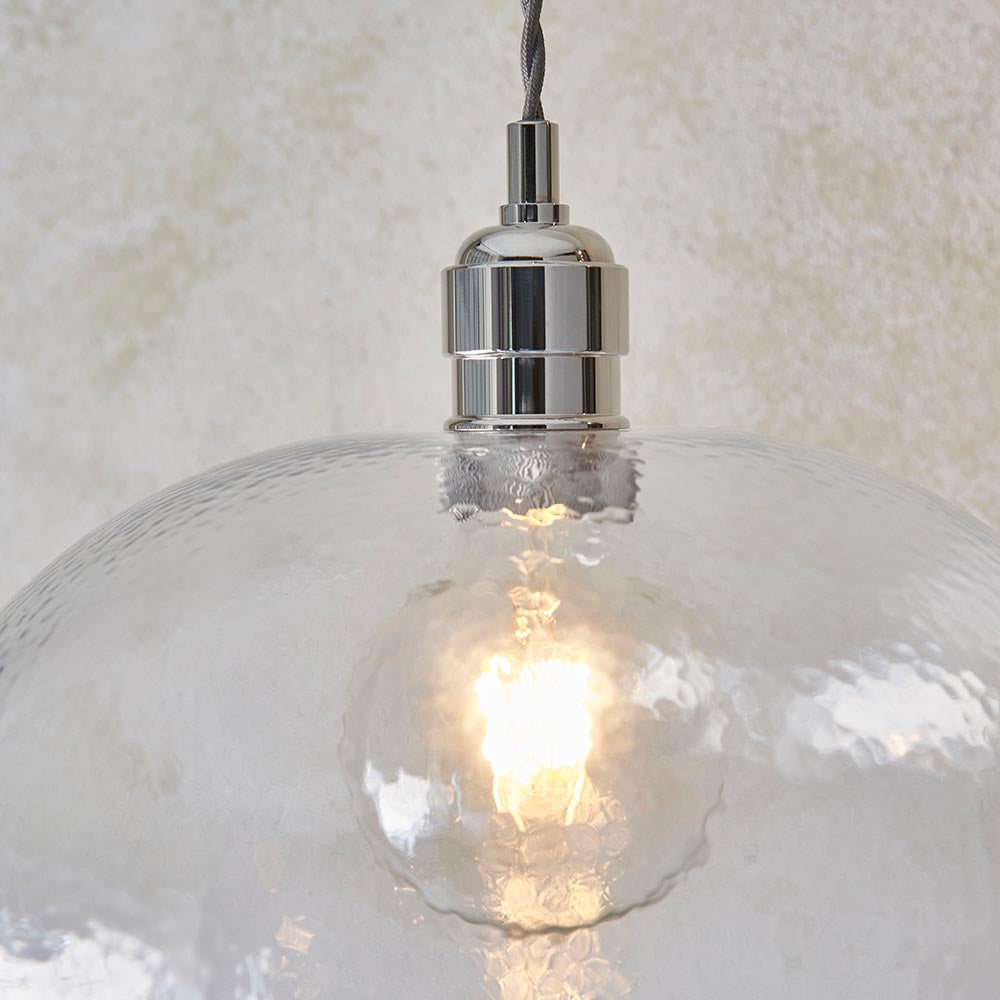 Close-up of the Lighting No.1 Draywick Hammered Medium Pendant in clear glass with bright nickel fitting, glowing E27 bulb visible through the dimpled shade.