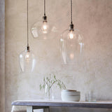 Trio of Lighting No.1 Draywick hammered clear glass pendants in bright nickel hung at varied drops above a dining table with vase and bowls.