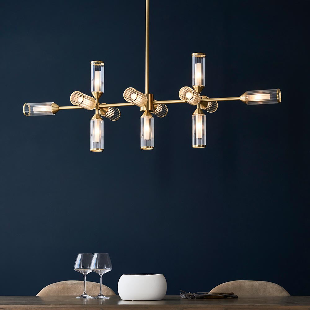 Gorsewell Ribbed Linear 13 Light Pendant in frosted satin brass, with ribbed glass shades on a horizontal bar, shown lit against a deep navy wall.