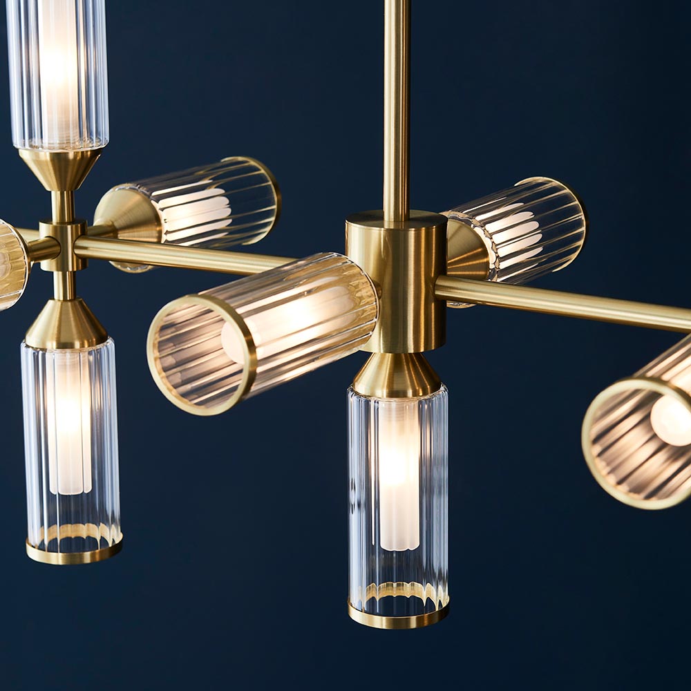 Close-up of the Gorsewell Ribbed Linear 13 Light Pendant in frosted satin brass, showing ribbed glass shades on brass arms against a deep navy background.