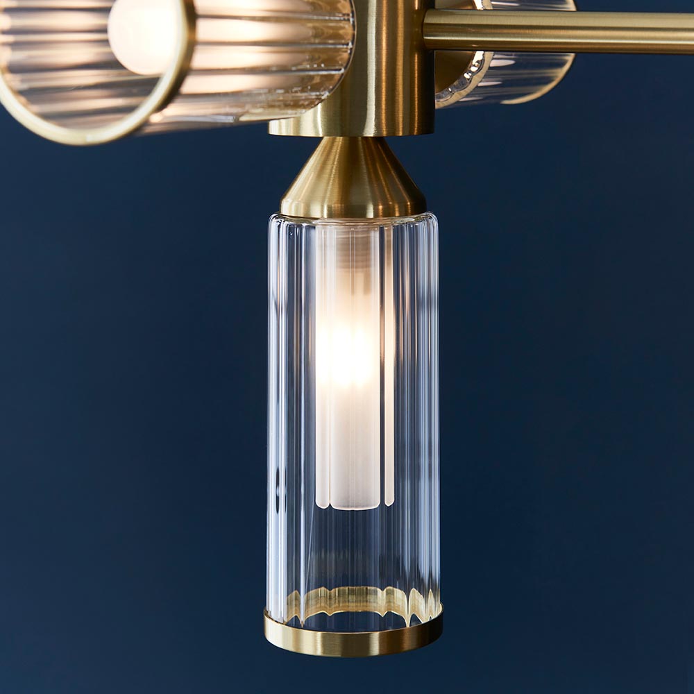 Close-up of Lighting No.1 Gorsewell Ribbed Linear pendant shade, a ribbed frosted glass cylinder with satin brass collar and lit G9 bulb, on deep blue.