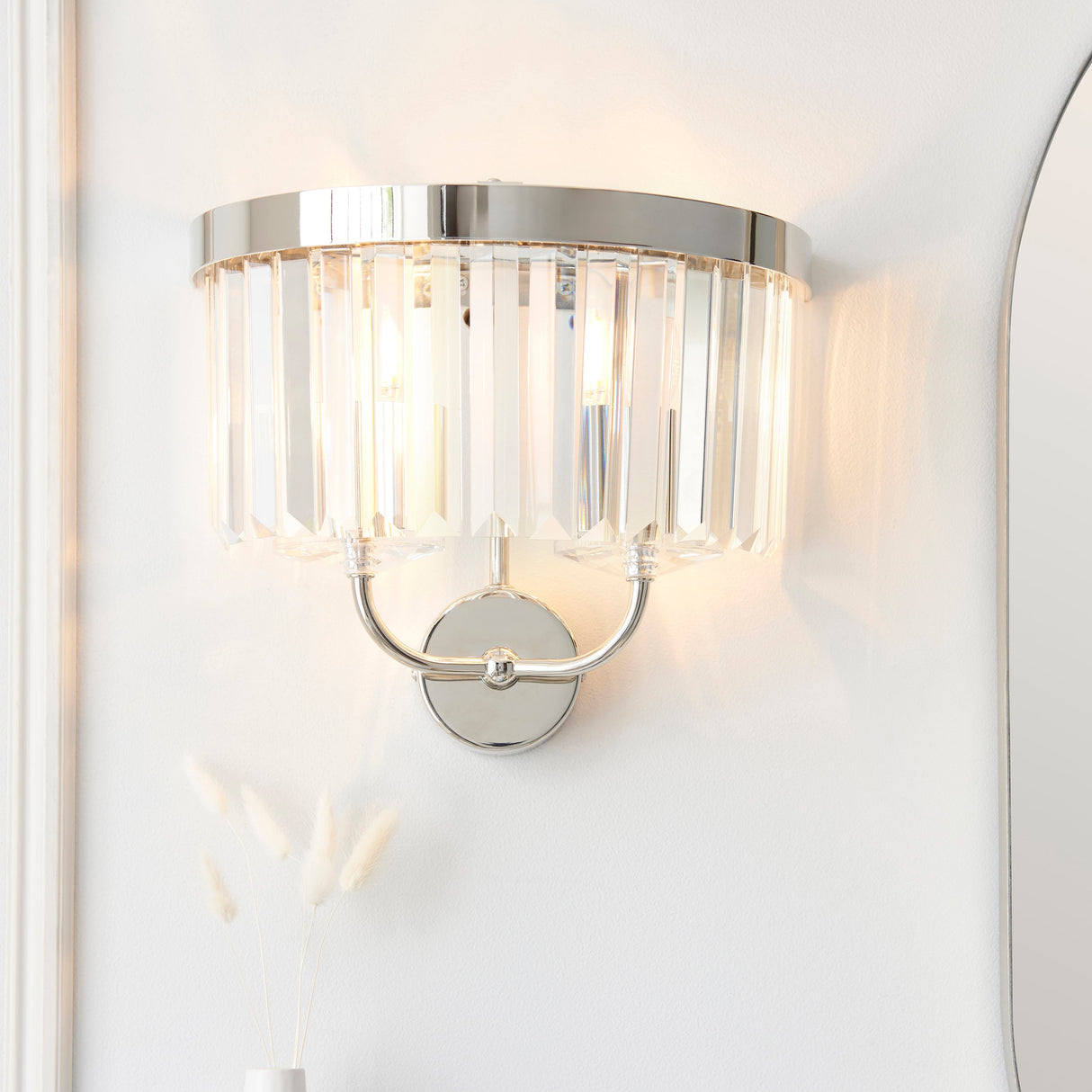 Calverdale Cut 2 light wall light in bright nickel with tiered faceted cut glass shades, illuminated on a white wall beside a mirror.