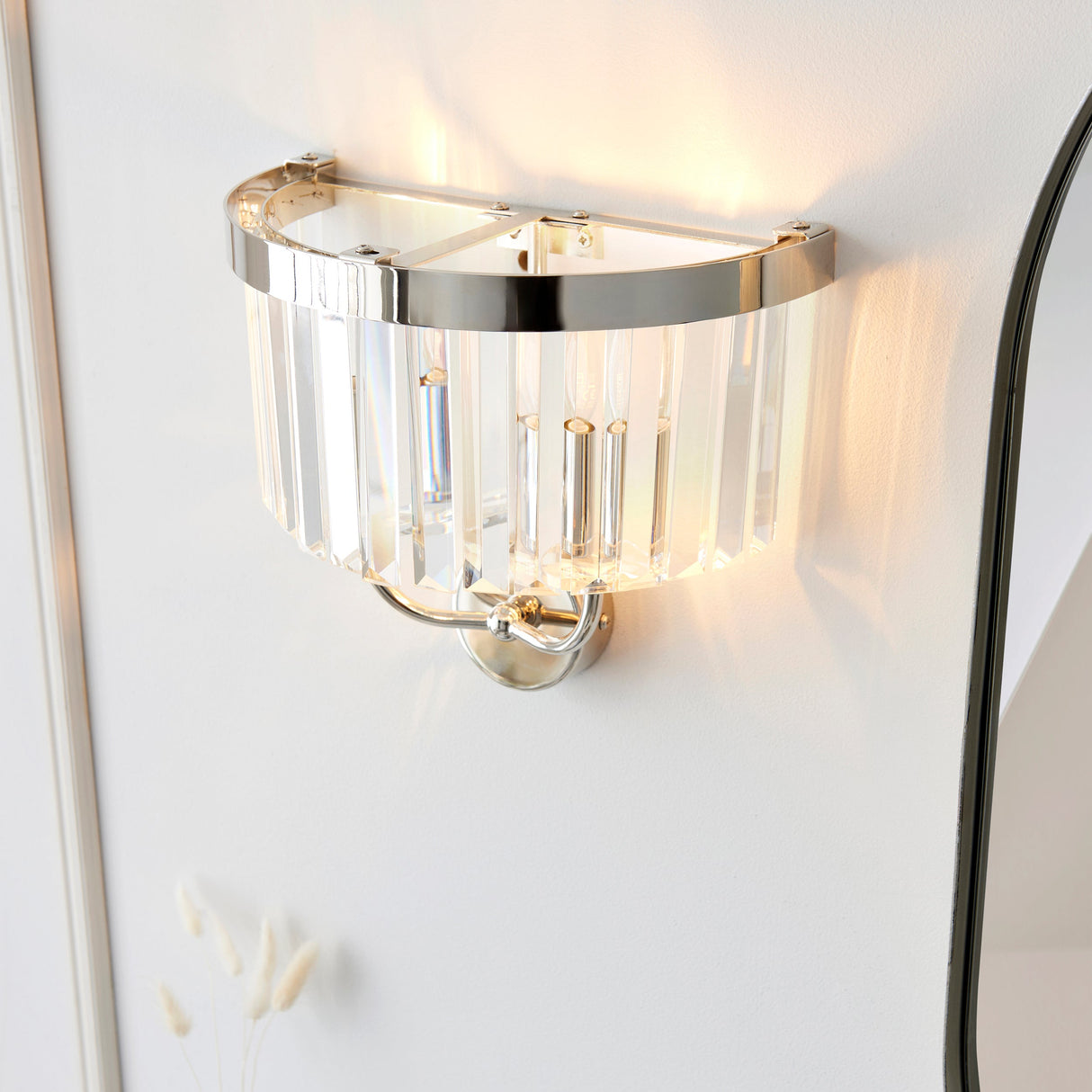 Calverdale Cut 2 light wall light in bright nickel with faceted cut glass shades, illuminated on a white wall beside an arched mirror.