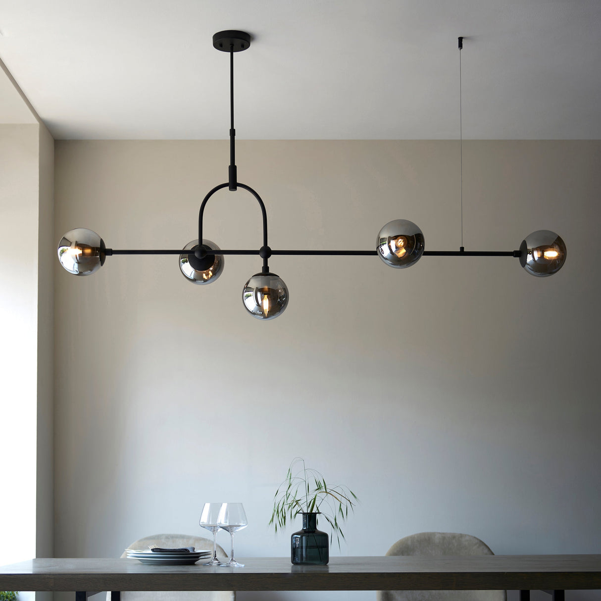 Lighting No.1 Haldmere linear 5-light pendant with smoked grey glass spheres on a matt black adjustable bar, shown above a dining table.