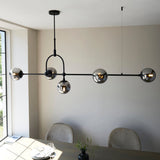 Lighting No.1 Haldmere linear pendant with five smoked grey glass spheres on a matt black bar and adjustable stem, above a dining table.