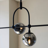Close-up of Lighting No.1 Haldmere linear pendant showing matt black arched stem and smoked grey tinted glass spheres with visible E14 filament bulb.