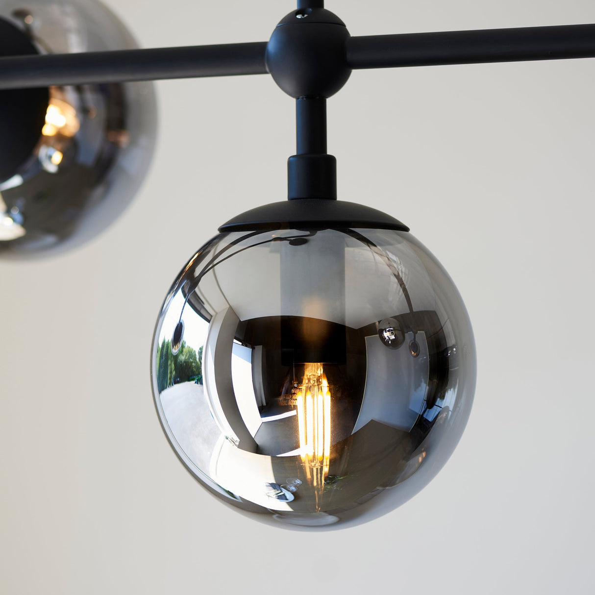 Close-up of the Lighting No.1 Haldmere pendant showing a smoked grey glass sphere with visible filament bulb on a matt black stem and bar.