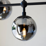 Close-up of the Lighting No.1 Haldmere pendant showing a smoked grey glass sphere with visible filament bulb on a matt black stem and bar.