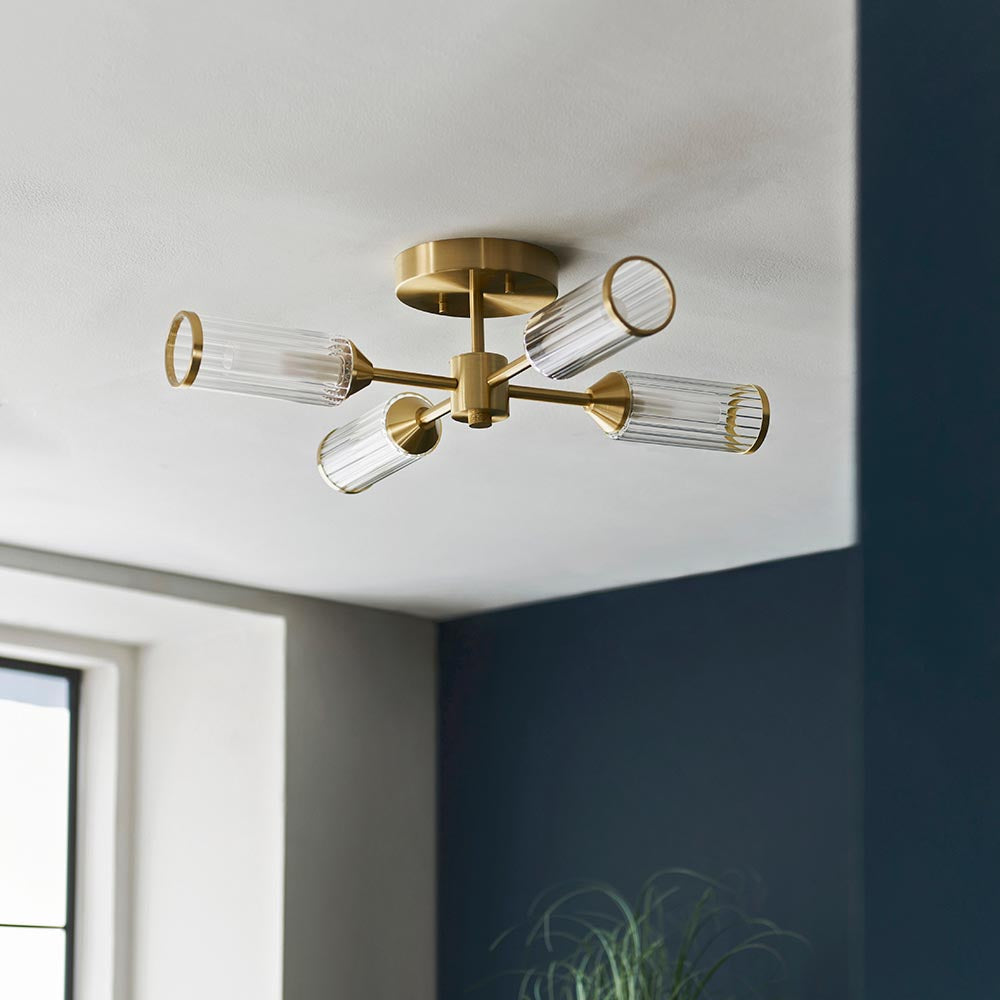 Gorsewell Ribbed Semi-flush 4 Light ceiling fitting in satin brass with frosted ribbed glass shades, mounted on a white ceiling beside a navy wall.