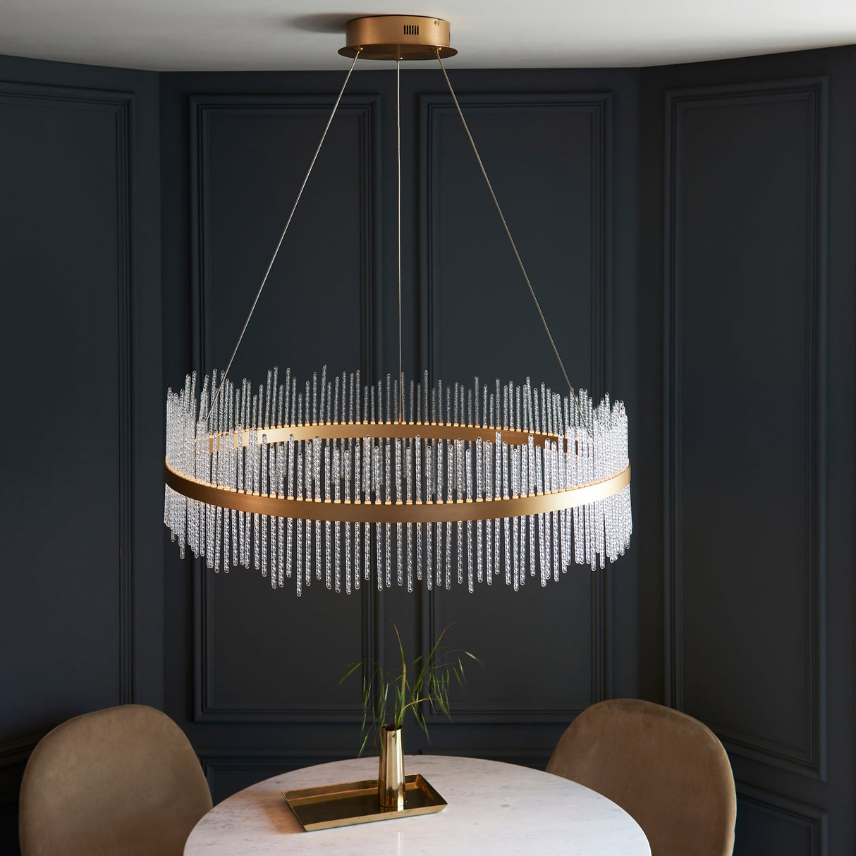Rookhurst Rod Grand Pendant in gold by Lighting No.1, a wide ring of clear glass rods suspended above a marble dining table in a panelled room.