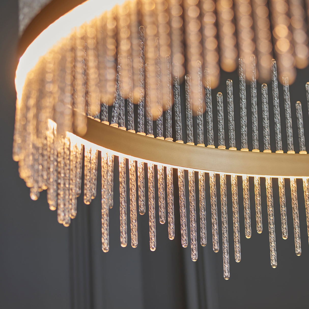 Close-up of the Lighting No.1 Rookhurst Rod Grand Pendant in gold, showing the curved gold frame and clear glass rods lit by warm integrated LED.