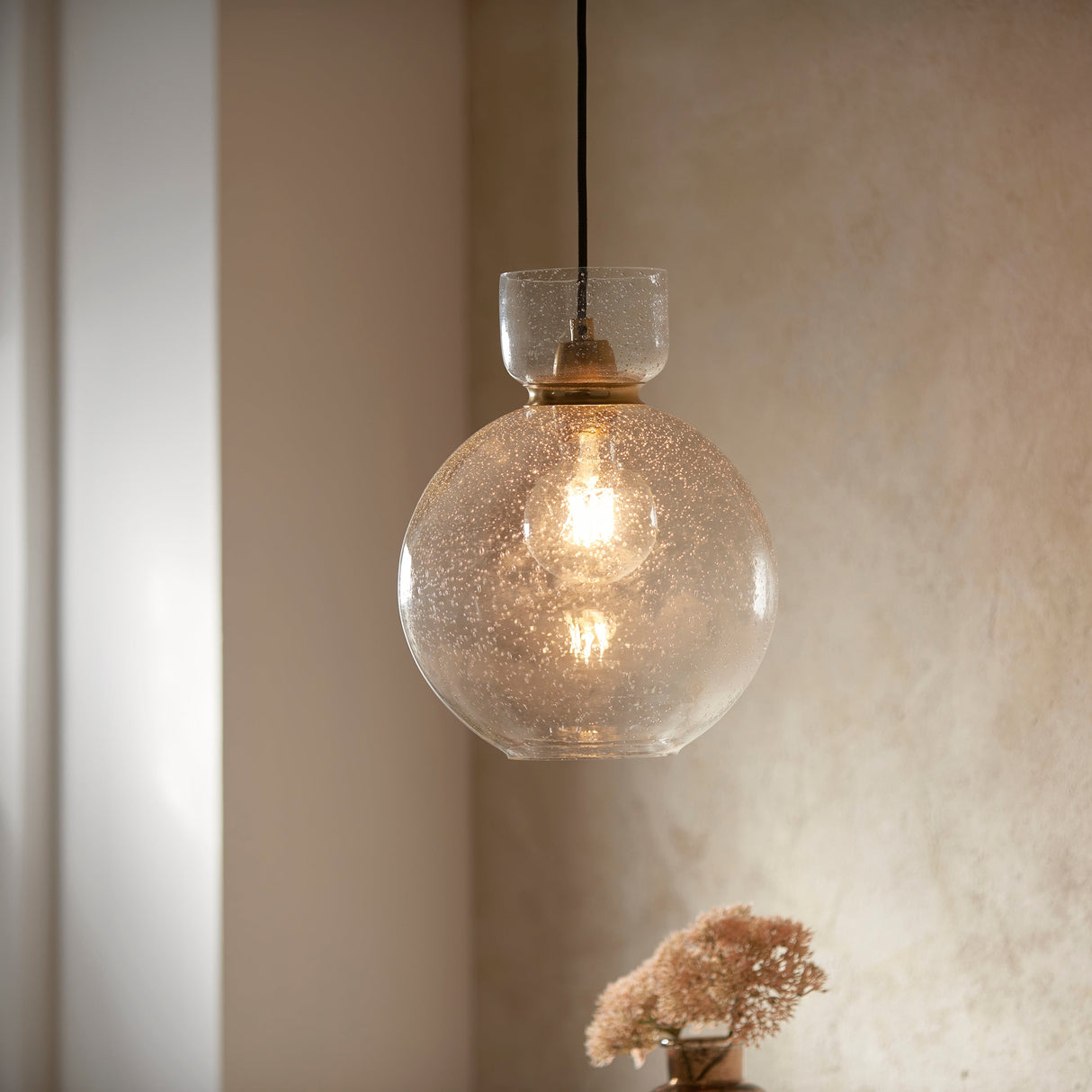 Yarnwell Bubble Pendant featuring a clear bubbled glass globe shade and exposed filament bulb, hanging from a black cable against a warm neutral wall.