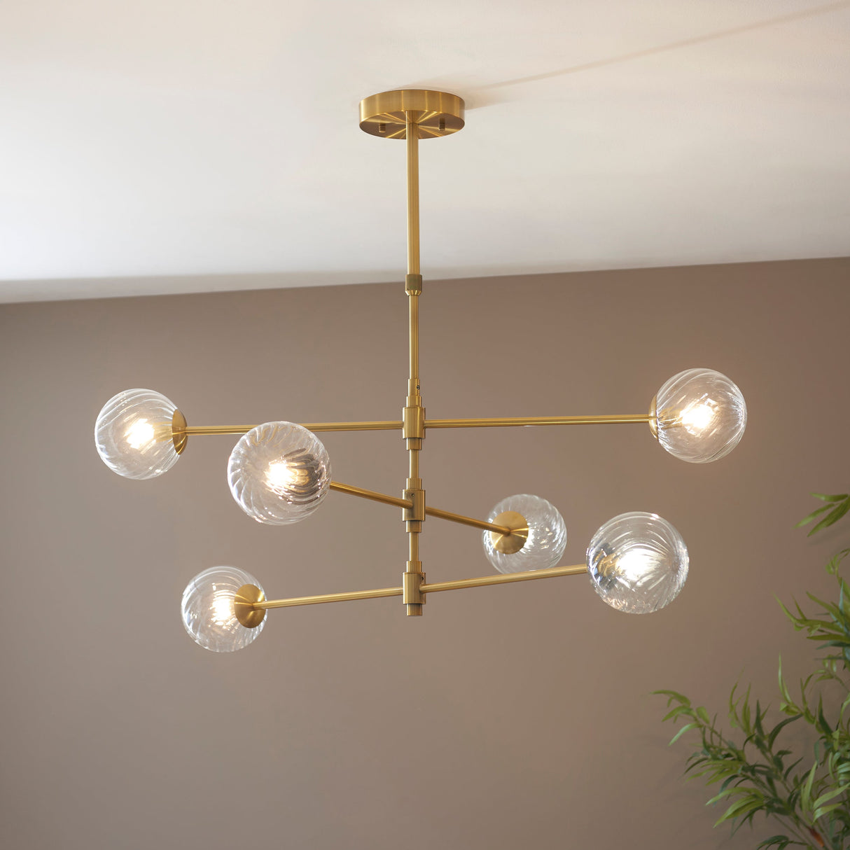 Lighting No.1 Mossgrove Twisted 6 Light Pendant in brushed aged brass with six twisted clear glass globes on splayed arms, mounted to a neutral ceiling.