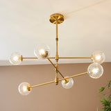 Mossgrove Twisted 6 Light Pendant in brushed aged brass with six angled arms holding twisted clear glass globe shades, mounted to a neutral ceiling.
