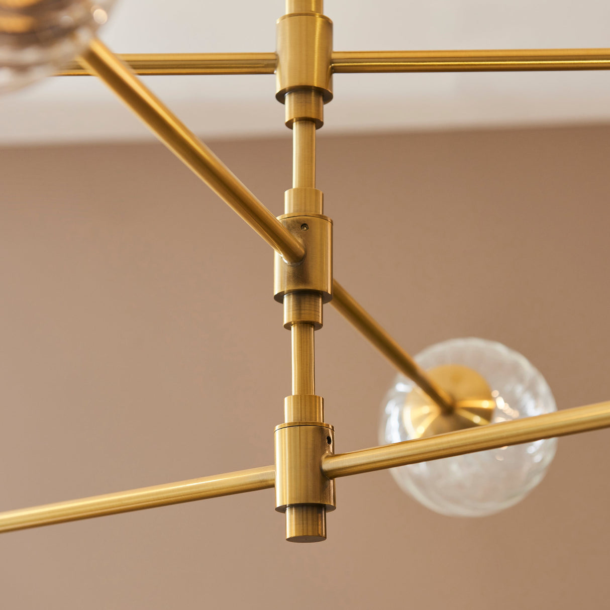Close-up of the Lighting No.1 Mossgrove Twisted 6 Light Pendant showing brushed aged brass arms, cylindrical joints and a clear glass shade.