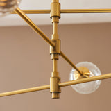 Close-up of the Lighting No.1 Mossgrove Twisted 6 Light Pendant showing brushed aged brass arms, cylindrical joints and a clear glass shade.