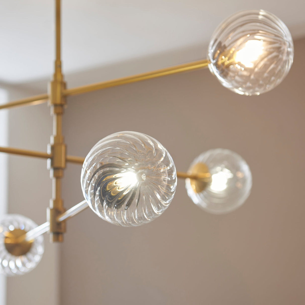 Close-up of the Lighting No.1 Mossgrove Twisted 6 Light Pendant, showing twisted clear glass globes on a brushed aged brass frame.