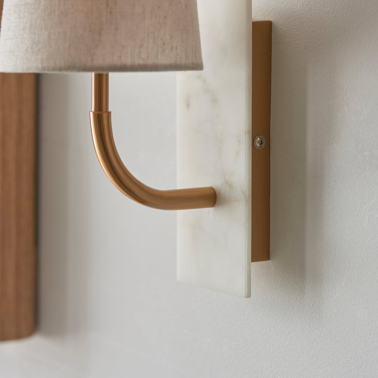 Close-up of the Lighting No.1 Fernhaven curved arm wall light, showing the vintage brass arm rising from a white marble backplate.