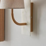 Close-up of the Lighting No.1 Fernhaven curved arm wall light, showing the vintage brass arm rising from a white marble backplate.