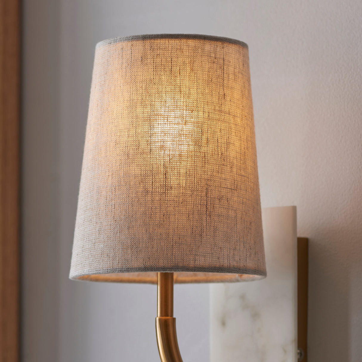Fernhaven vintage curved arm tapered wall light by Lighting No.1, close-up of the linen tapered shade lit warmly above a brass arm and white marble plate.