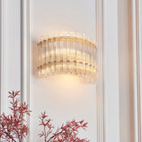 Nettlecote 2 light wall light by Lighting No.1, illuminated with clear glass rods in a brushed aged brass frame, mounted on a white panelled wall.