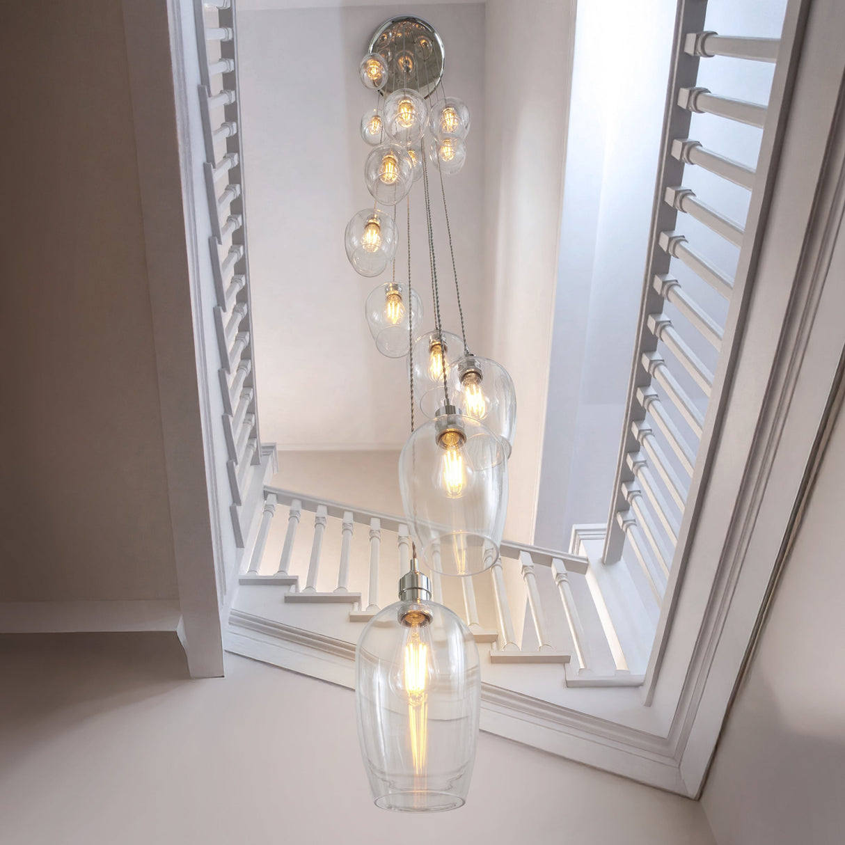 Quilbrook Cascade 13 light pendant from Lighting No.1 with clear glass globes spiralling from a bright nickel plate down a white stairwell.