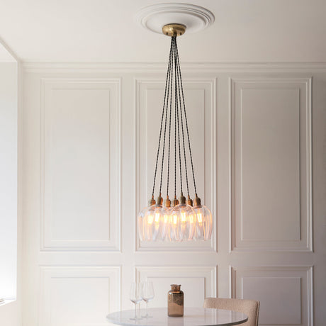Quilbrook Cluster 7 Light Pendant in antique brass with clear glass globes, hung from a ceiling rose above a marble table in a panelled dining room.