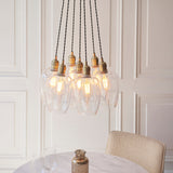 Lighting No.1 Quilbrook cluster pendant with seven clear glass globes and antique brass holders on twisted cords, lit above a marble dining table.
